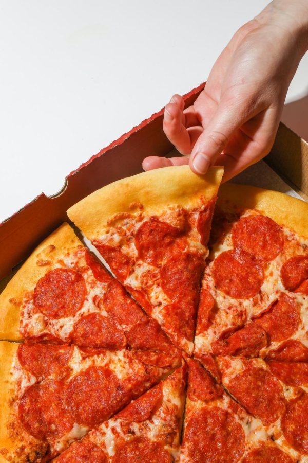 Photo of hand grabbing for slice of pizza from box.