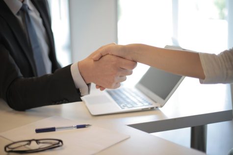 Two people shake hands over desk with laptop and pen in background