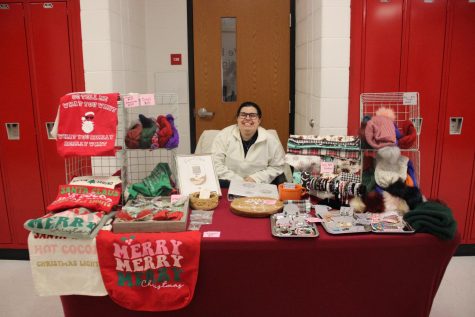 Craft vendor sitting behind her table with her holiday crafts displayed all around. 