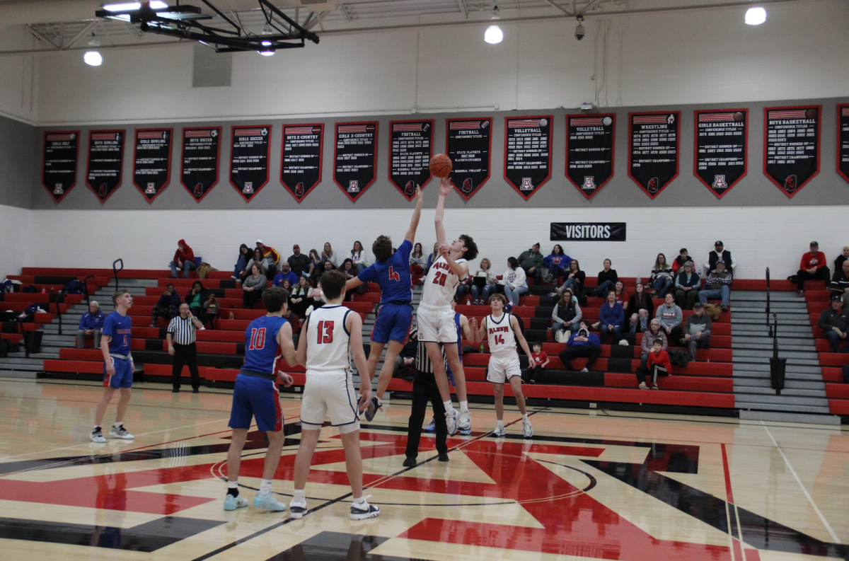 Junior Sam Cramer jumps up with an opposing team member at center court at the beginning of the game. 