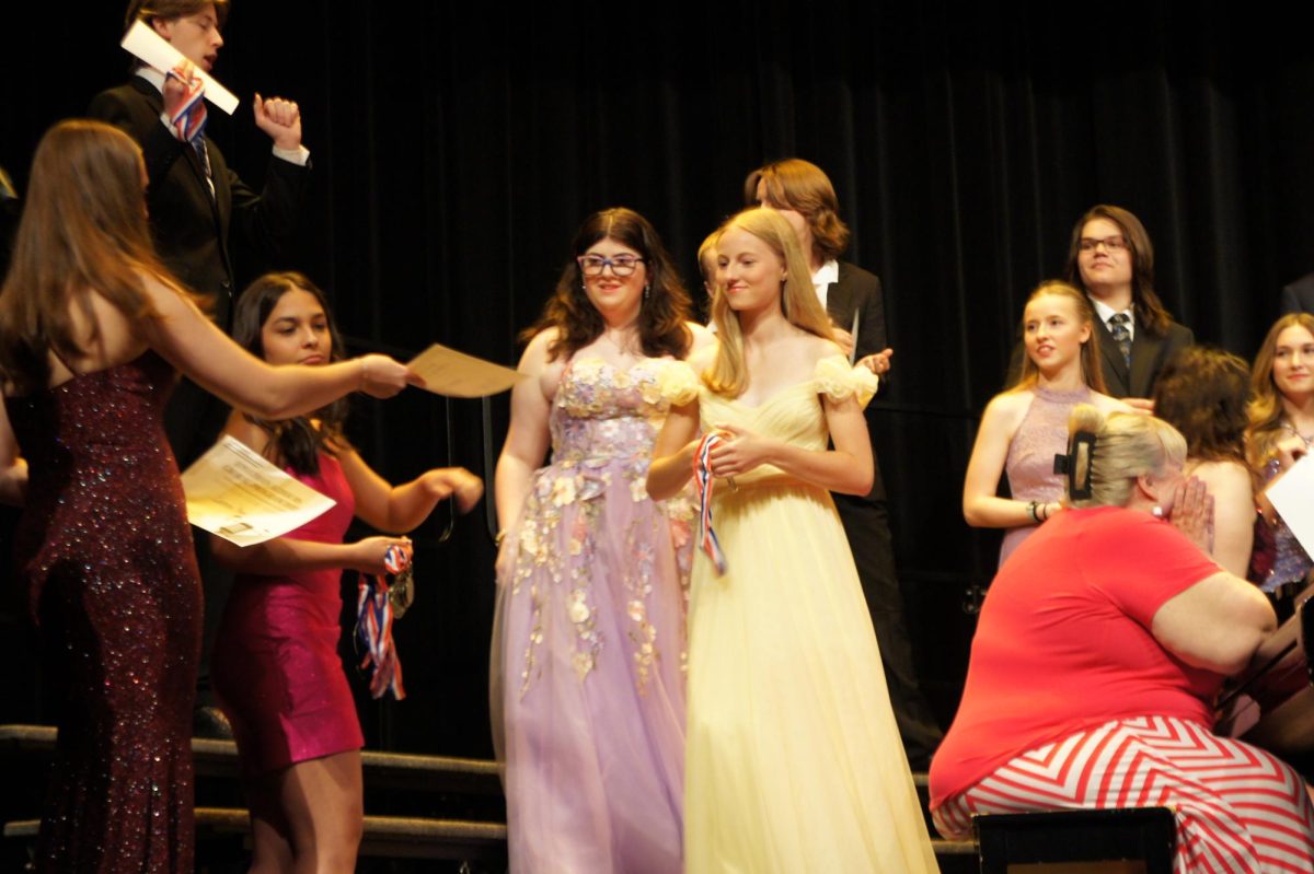 Sophomore's Avery Tyson and Gianna Cazares give senior Amanda Simmons her reward and metal.