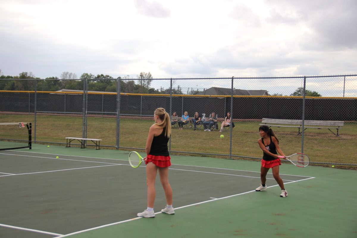 Flores-VIllanueva serves in a doubles warmup with senior Audrey Manring.