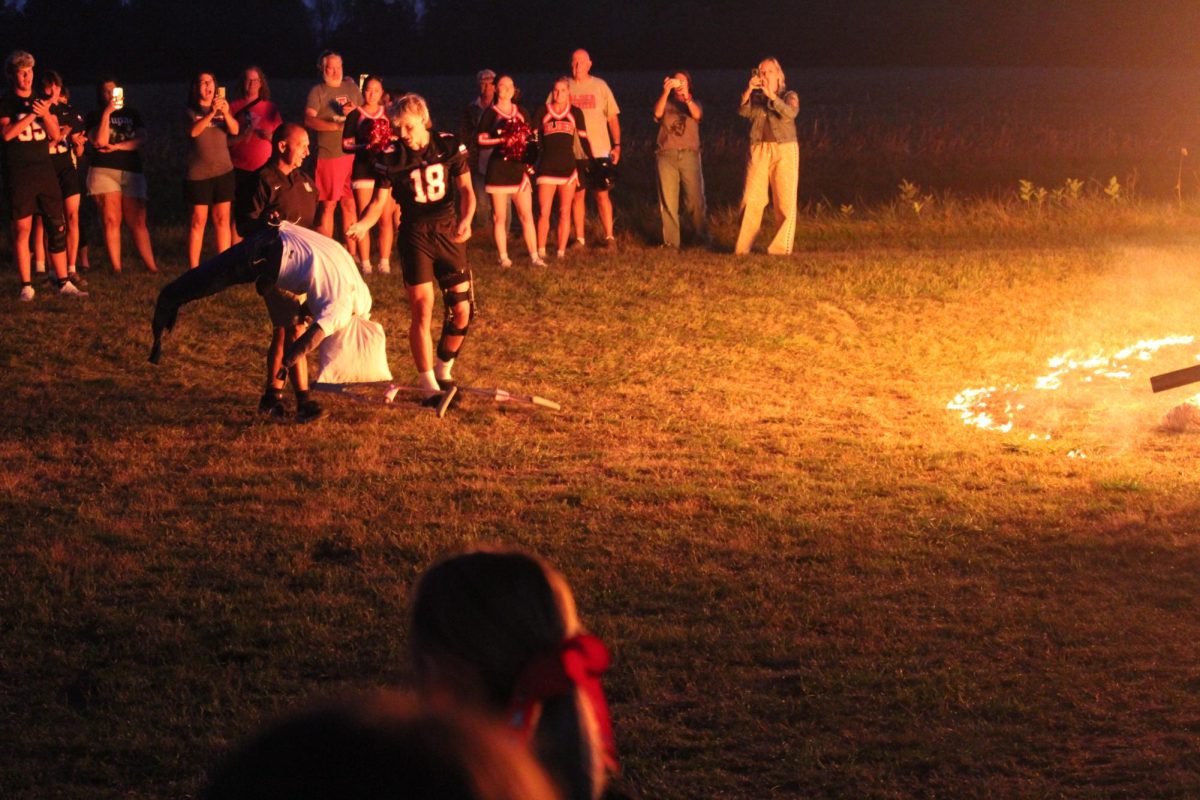 Assistant varsity football coach Donnie Glick assists senior Blake Hardy in throwing the dummies into the fire. 