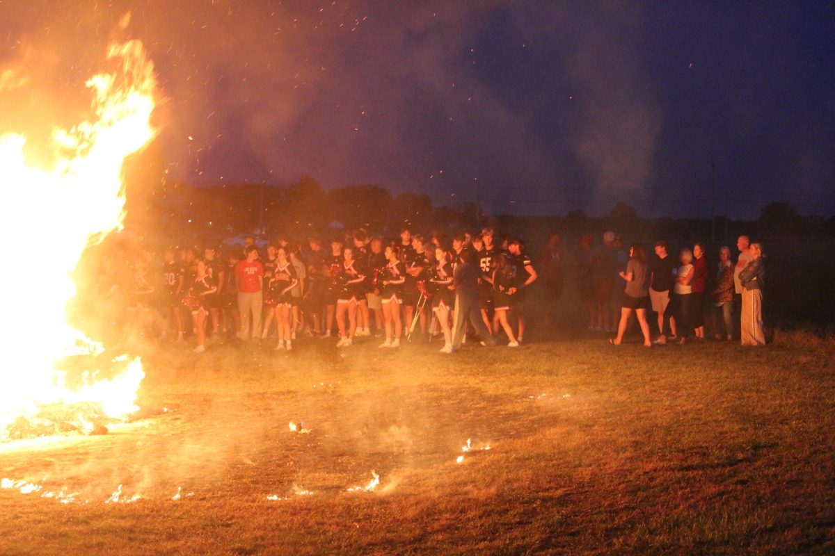 Football seniors and cheer teams stand in the glow of the raging bonfire.